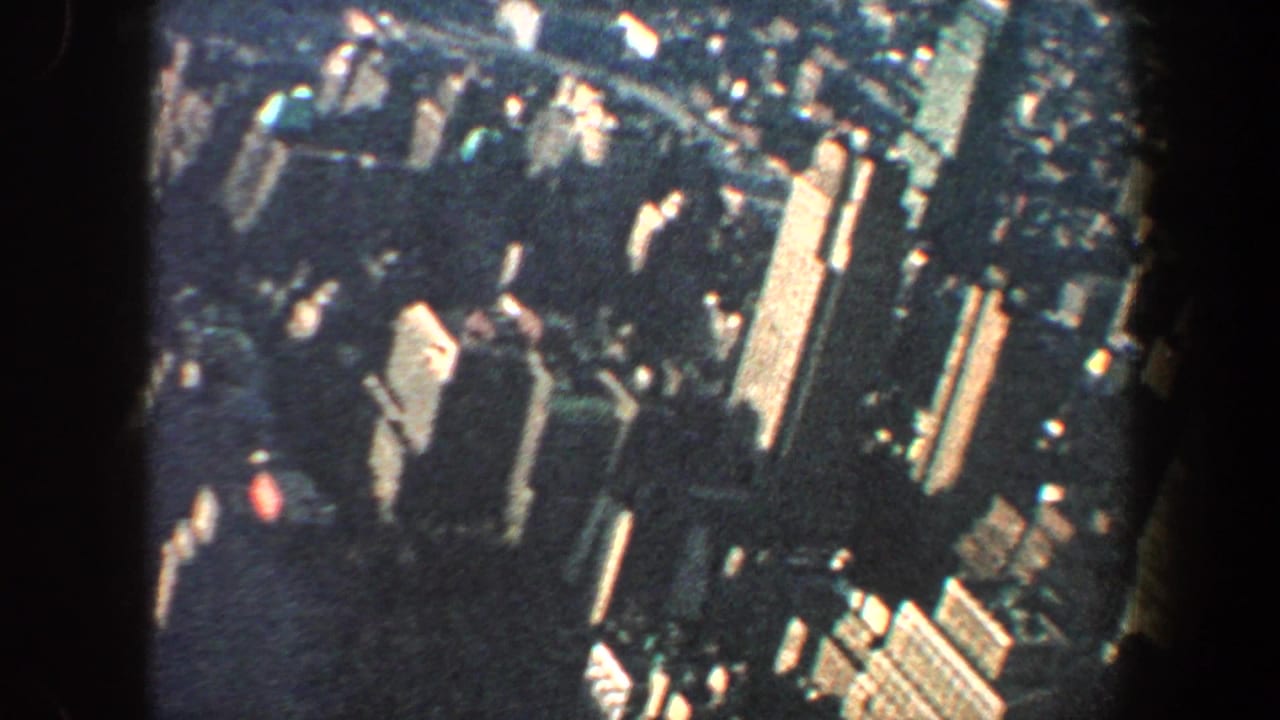Aerial city view with clustered high-rises, streets, and bright building facades.