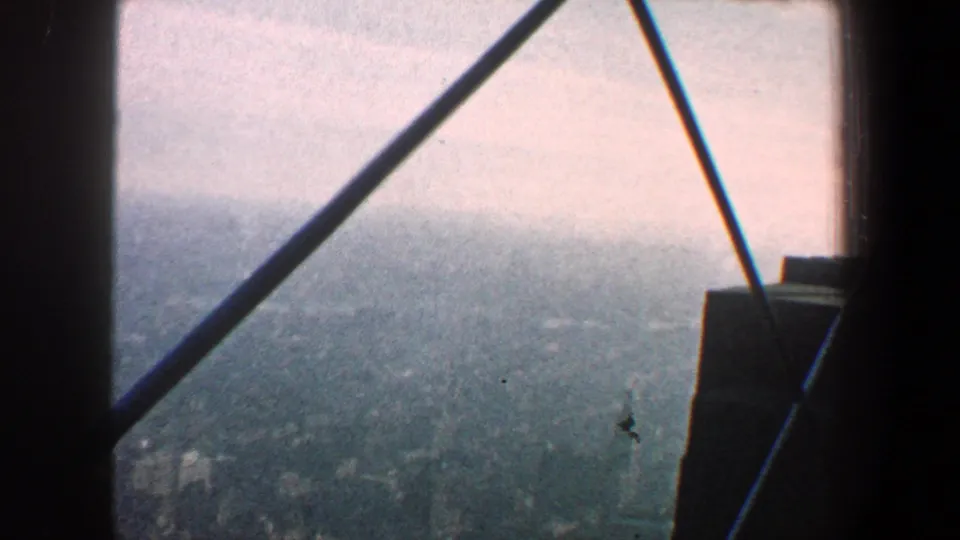 1960 New York City elevated view through dark beams, looking toward a hazy river or distant urban horizon.