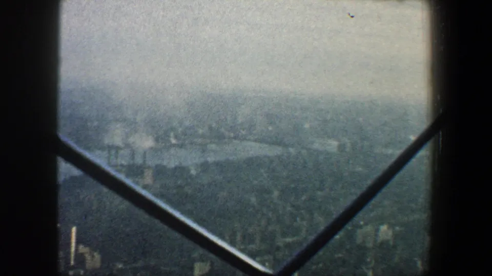 Elevated 1960 New York City view with water, shoreline structures, and distant buildings seen through window framing.