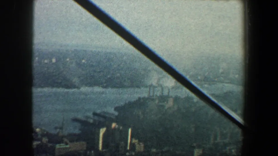 1960 New York City home-movie frame showing a hazy elevated view of water, dense buildings, and a diagonal structural beam.
