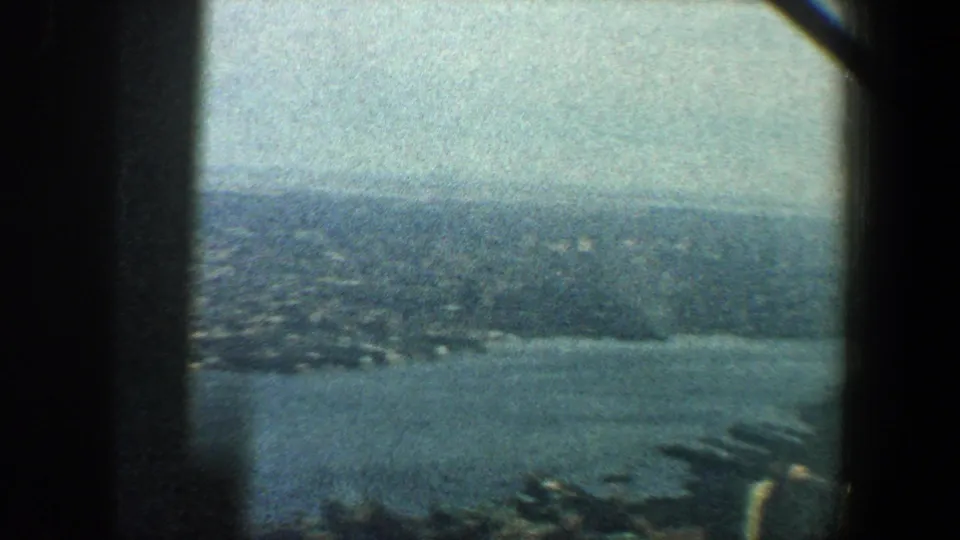 1960 New York City frame showing a hazy high-angle view over water toward a distant shoreline and rooftops.