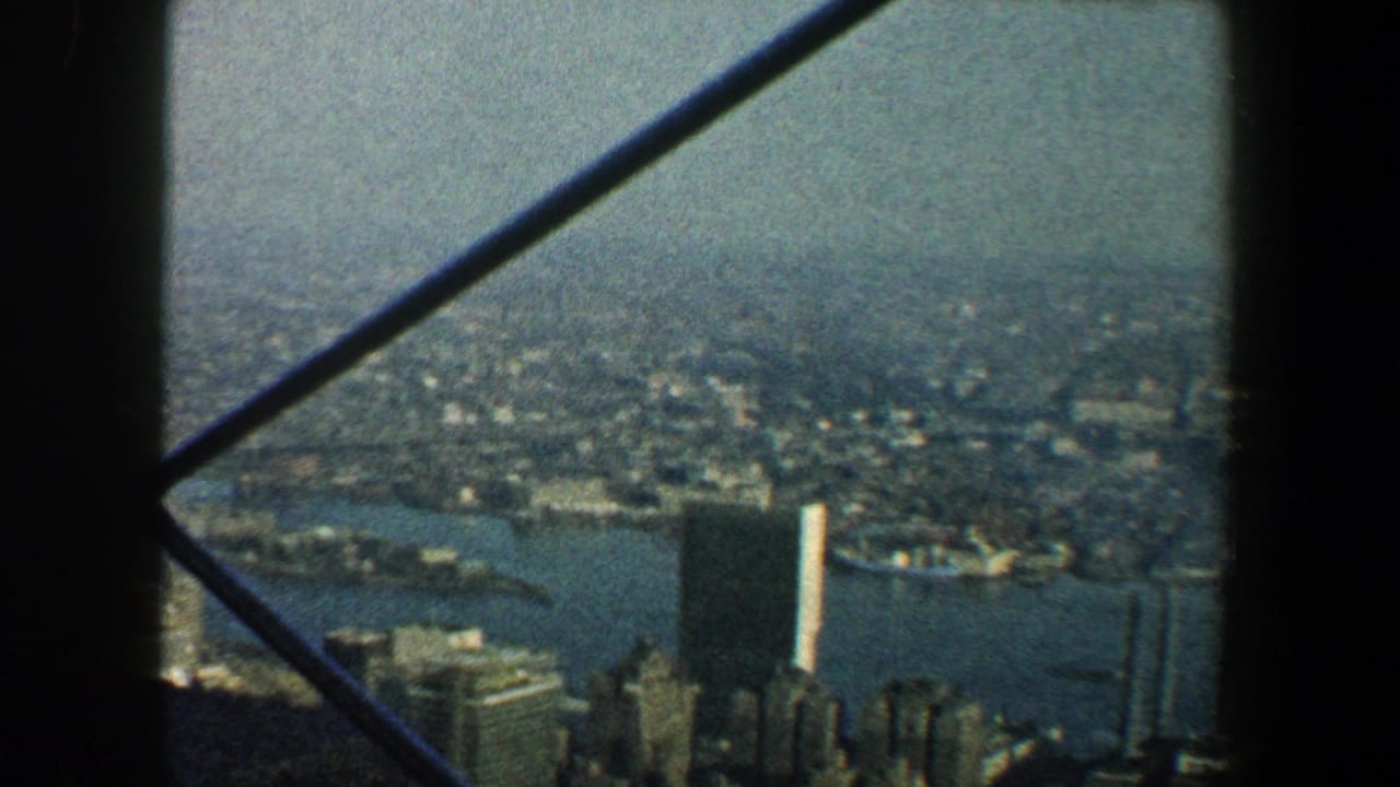 High view over New York City buildings and river water, partly framed by dark structural bars.
