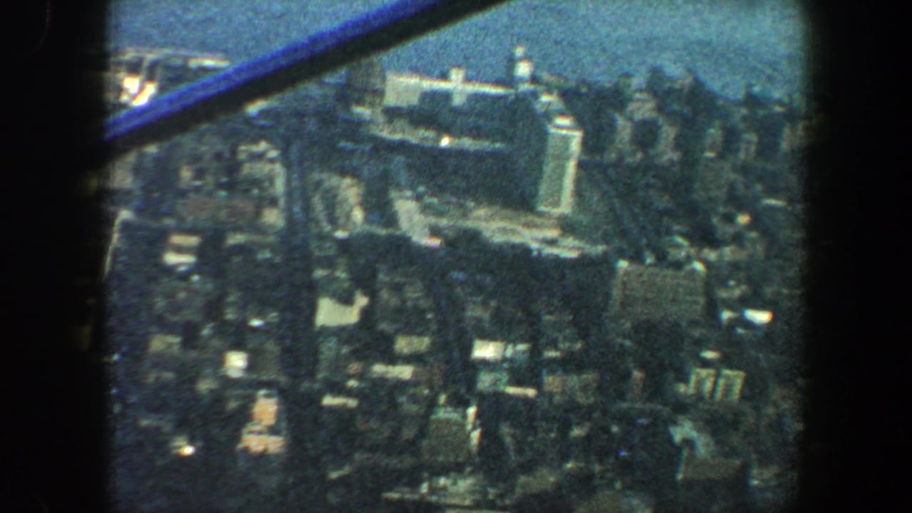 1960 New York City home-movie view over high-rise blocks and a broad river, framed by dark observation-deck structure.