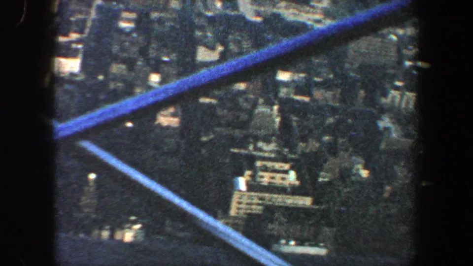1960 New York City aerial frame with shadowed urban blocks, scattered bright roofs, and aircraft struts visible.
