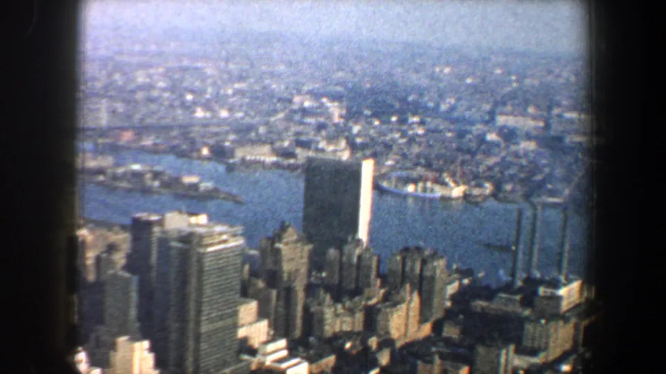 1960 New York City aerial view over waterfront towers, blue waterways, bridges, and a hazy urban horizon.