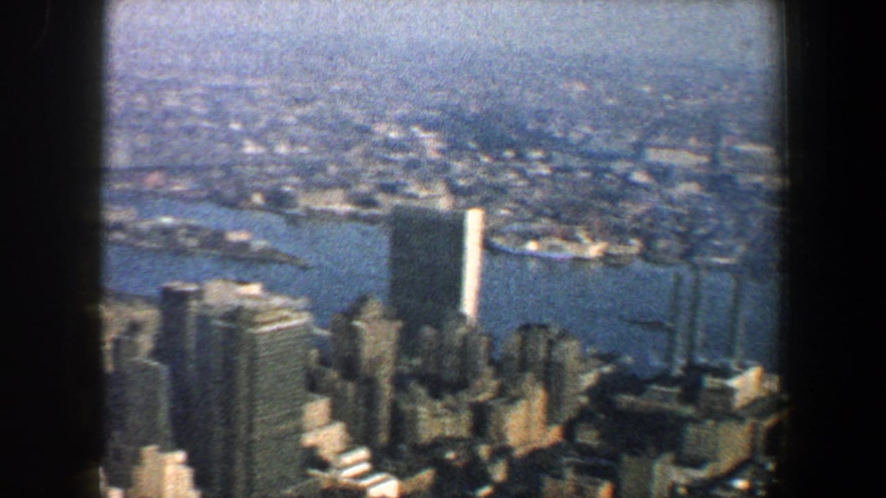 1960 New York City skyline viewed from above through dark window framing, with riverfront piers and tall buildings visible.