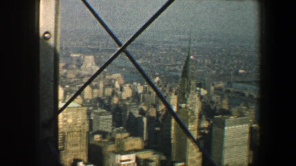 1960 New York City skyline with a pointed tower, nearby high-rises, river beyond, and crossed bracing in the foreground.