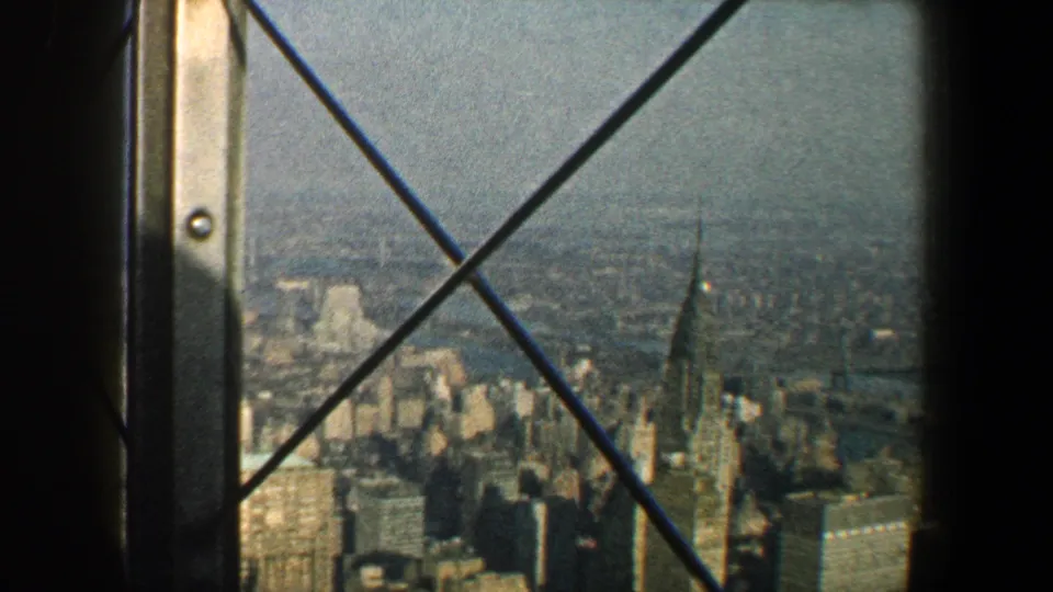 1960 New York City skyline with the Chrysler Building visible through an iron-barred high observation window.