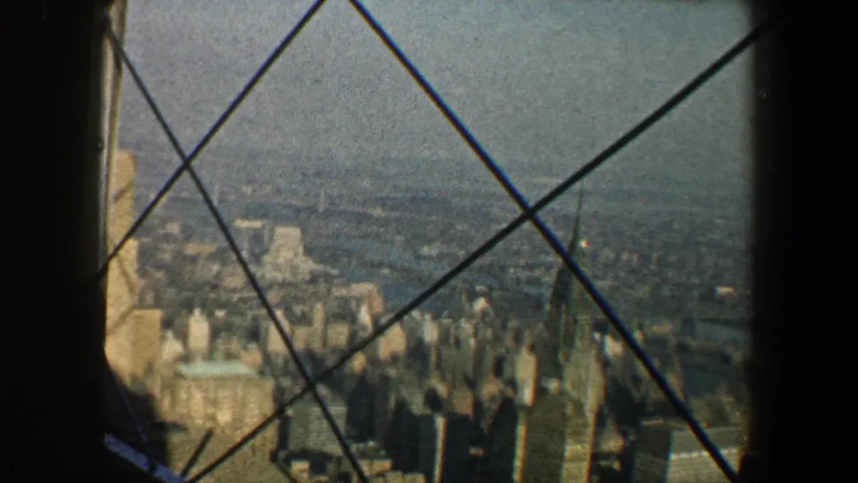 1960 New York City panorama with mid-century towers, a distant river, and crossed iron bars in the foreground.
