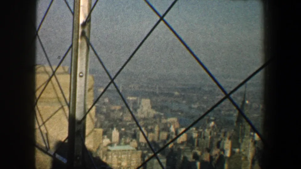 High vantage view over New York City in 1960, with iron bars and window framing over a hazy urban panorama.