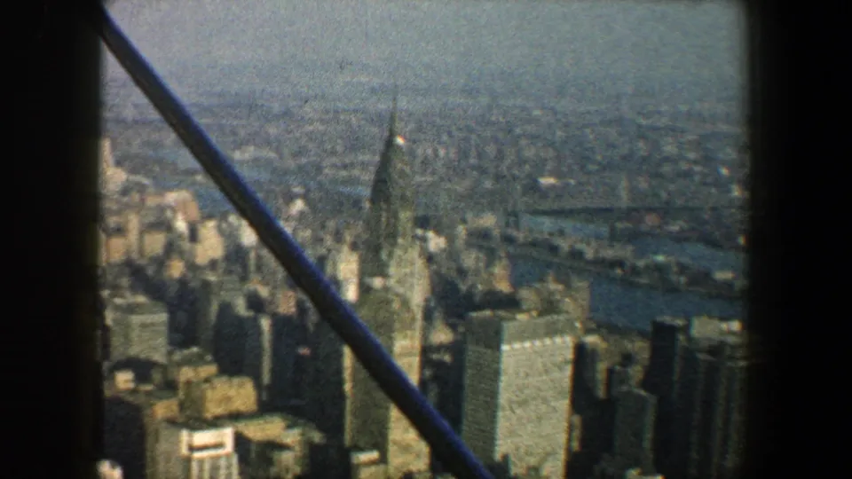 1960 New York City skyline view with the Chrysler Building prominent among mid-century towers, seen through dark foreground framing.