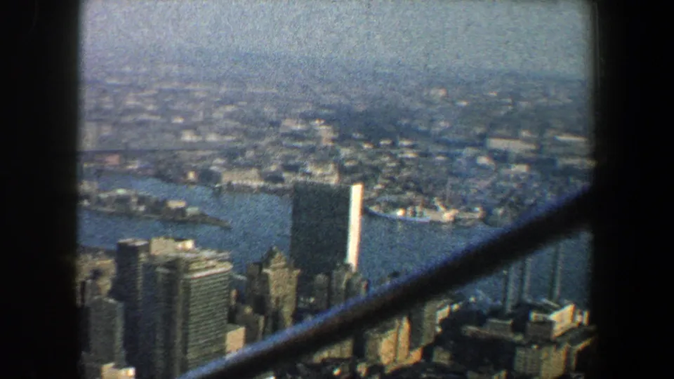 A high 1960 New York City view looks over the East River, waterfront buildings, distant bridges, and hazy urban horizon.