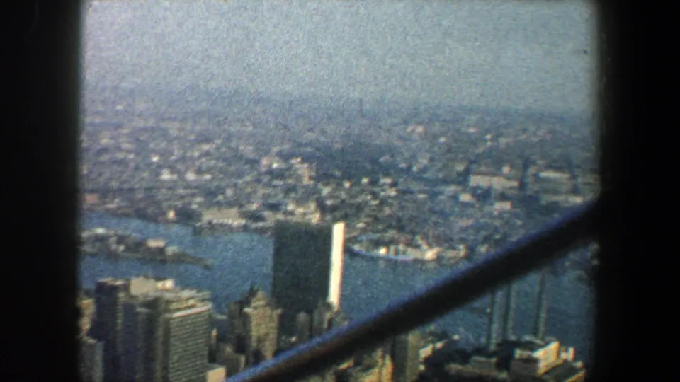 1960 8mm view over New York City buildings and waterfront from a high structure, crossed by dark vertical and diagonal beams.