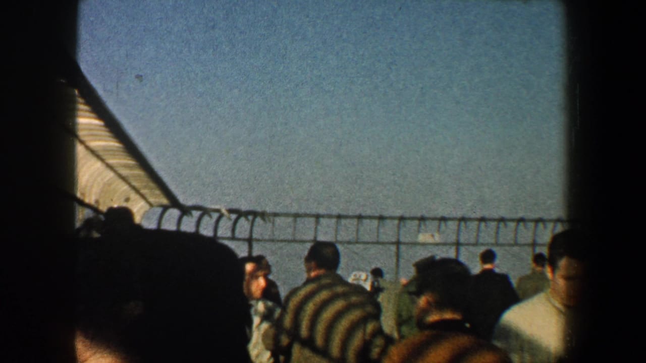 People in coats stand and walk near a fenced railing with open sky beyond.