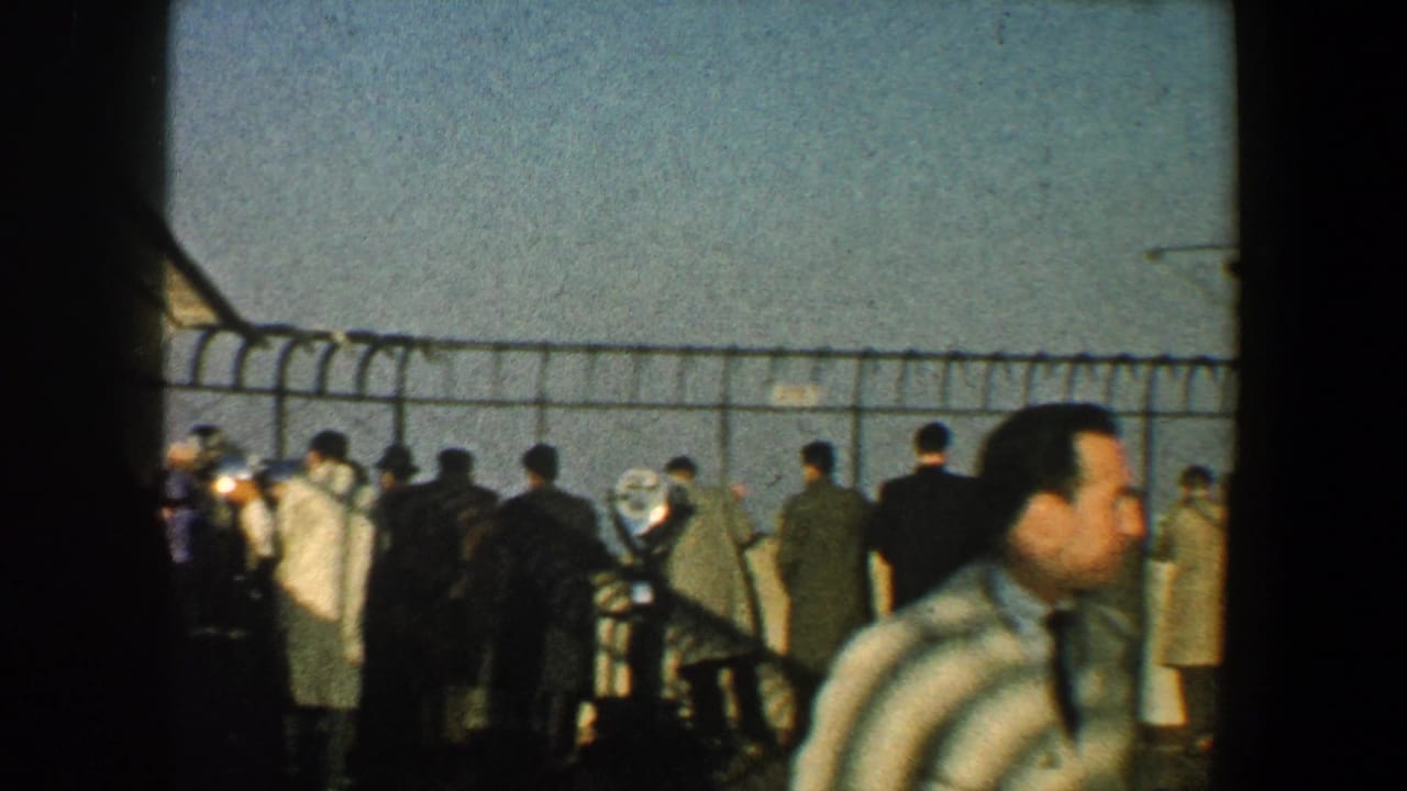 People gather near the observation-deck fence beside a dark structural post and windowed wall.