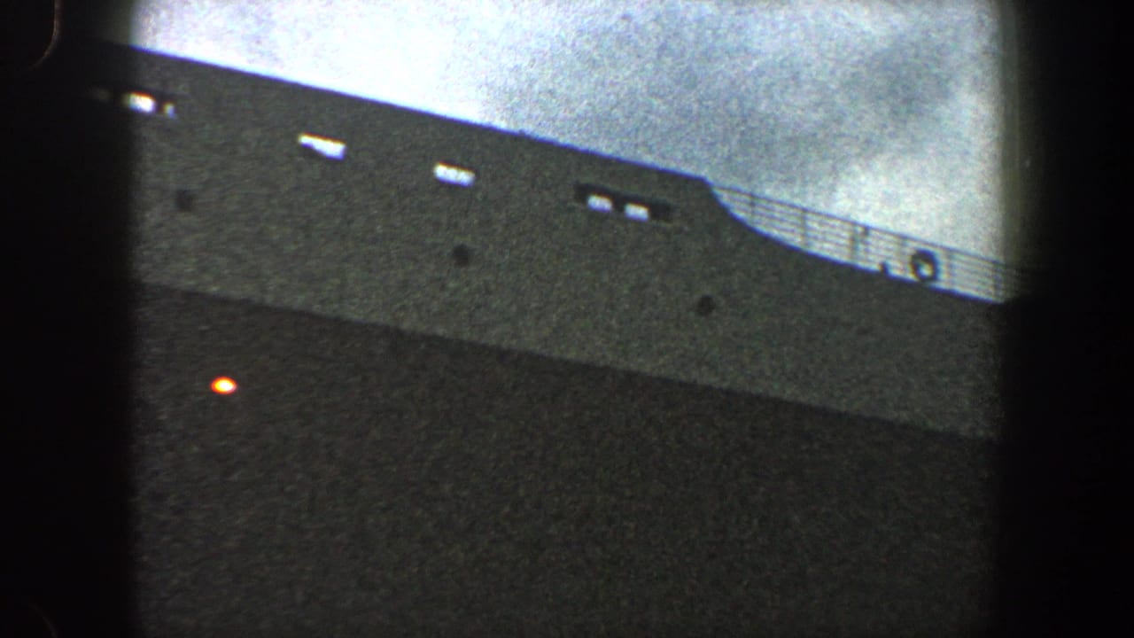 1960 New York City 8mm frame showing a gray ocean liner hull, deck railing, small openings, and an orange light.