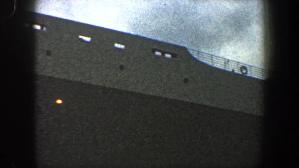 1960 New York City 8mm frame showing a gray ocean liner hull, deck railing, small openings, and an orange light.