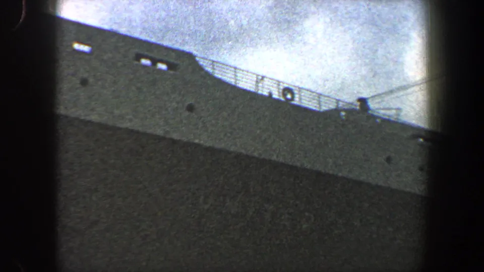 1960 New York City 8mm view of a large gray ship hull and upper deck railings against a cloudy sky.