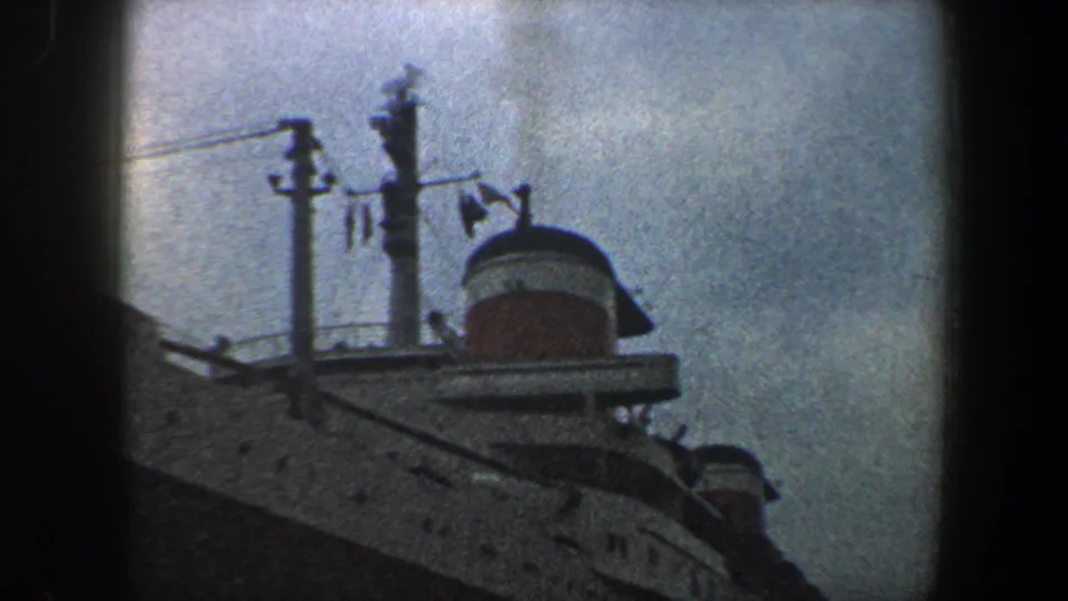 1960 New York City harbor footage frame with the ship's funnel, railings, masts, and white hull partly obscured by film-frame shadows.