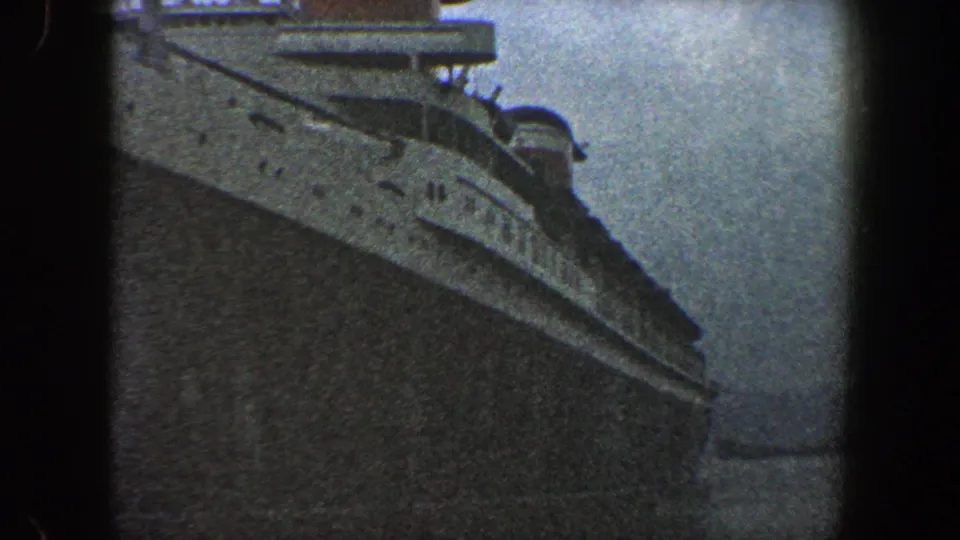1960 New York City home-movie frame showing a massive passenger ship hull from close below, with upper decks and railings visible.