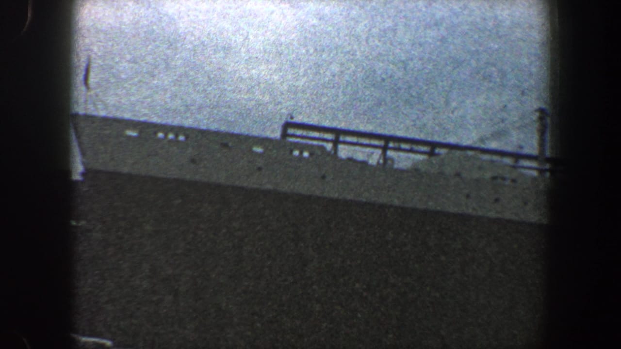 Distant ship deck and railings silhouetted beneath a pale hazy sky.
