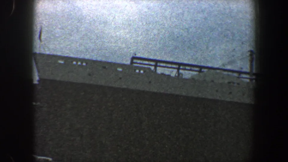 Distant ship seen in hazy 1960 New York City home-movie footage, with deck railings and dark foreground framing.