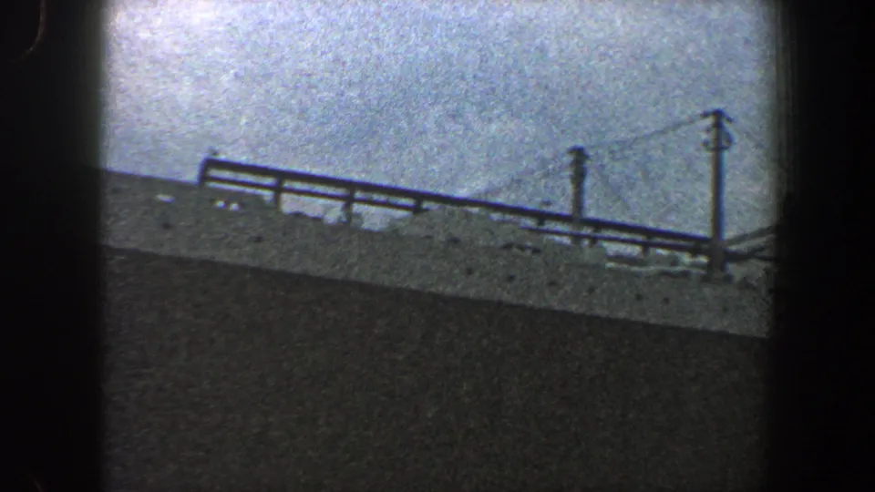 Grainy 8mm view of a ship in New York City, showing railings, deck edge, and vertical stack-like structures in haze.
