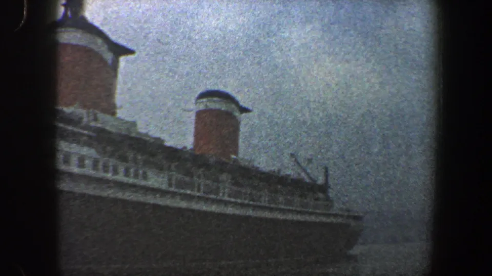 The pan continues across the ocean liner's upper decks, with red-and-white funnels and muted harbor light visible.