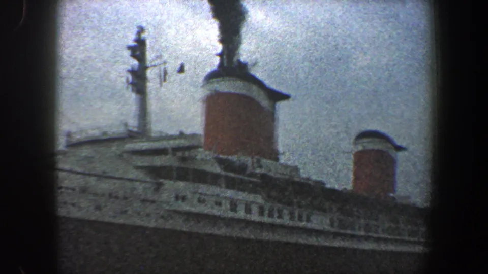 Near the end of the pan, black smoke rises from the taller funnel above the liner's decks in New York City harbor.