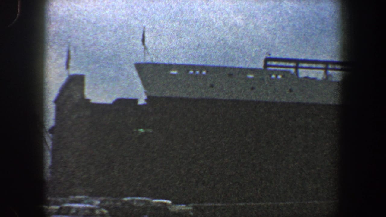 Large ocean liner docked beside a pier under a cloudy sky.