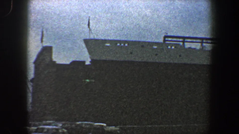 1960 New York City home-movie view of a large ocean liner at the port, framed from street level with the hull and upper deck visible.