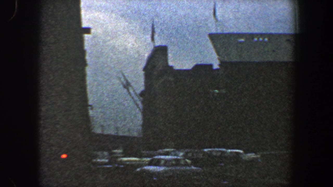 Pier-side view of a large ship with cars parked below.