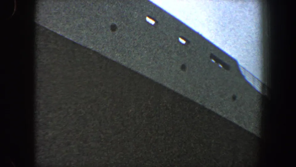Upward-looking 8mm view of a large ship side in New York City, with light openings and dark marks visible near the upper hull.