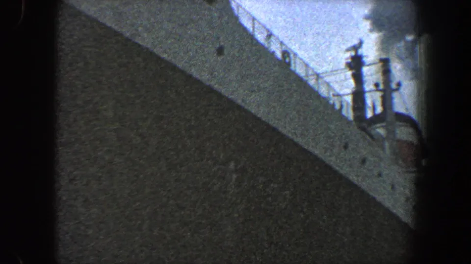 New York City 1960 8mm frame showing a large vessel side, deck railing, and a small person standing near the rail at right.