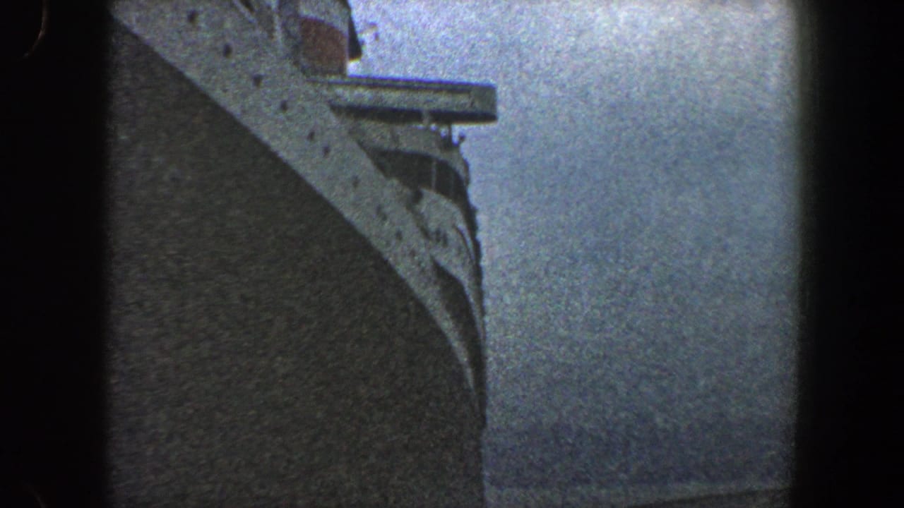 1960 New York City 8mm view looking beside a massive ship bow toward calm water, framed with dark film borders.