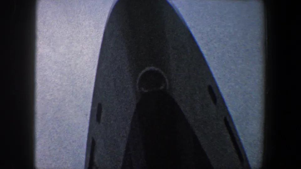 Upward 8mm view of the ship bow, with a round opening and dark hull surface against pale sky in New York City.