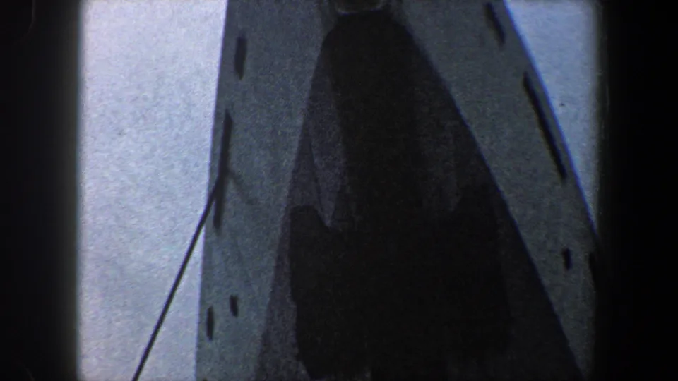 Close 1960 8mm view of the ocean liner bow with dark opening, small hull details, and a line crossing the bright sky.