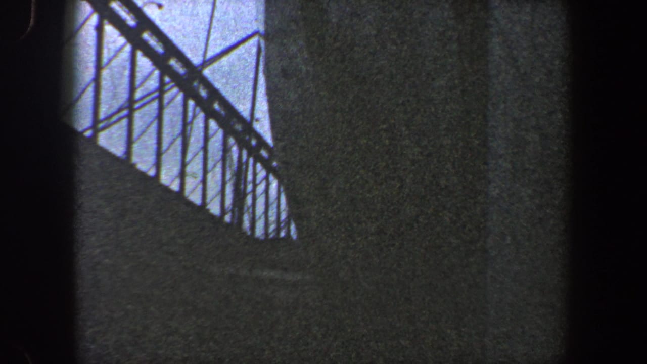 Low-angle close view of a dark grey ship hull with railings against a cloudy sky.