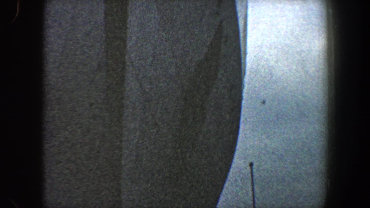Dark ship hull beside pale sky with film grain and black frame edges.
