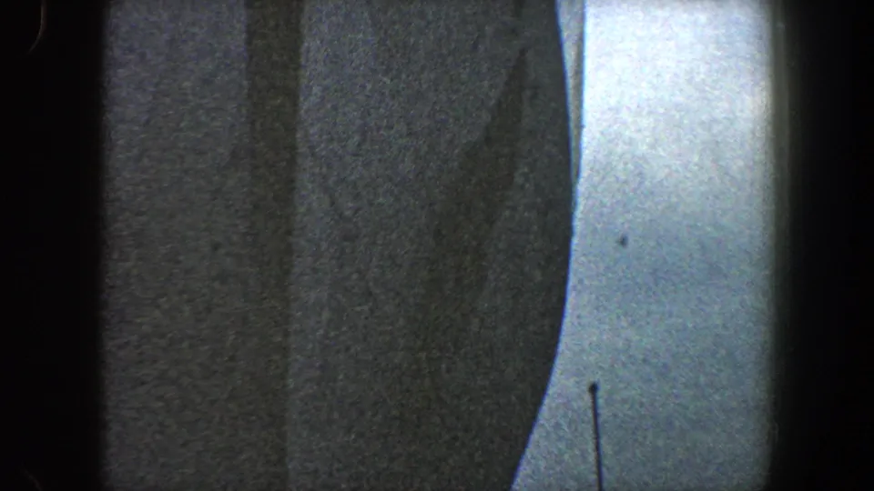 1960 New York City harbor footage showing a close dark ship hull against a pale sky, with soft 8mm grain and frame-edge shadows.
