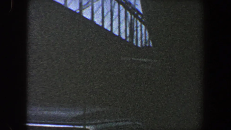 1960 New York City home-movie frame with a shadowed bridge surface and steel trusswork silhouetted near the sky.