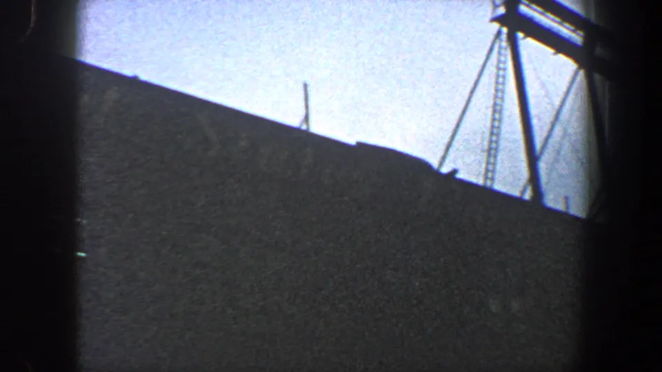 1960 New York City 8mm frame showing the edge of a bridge under construction with crane-like rigging against the sky.