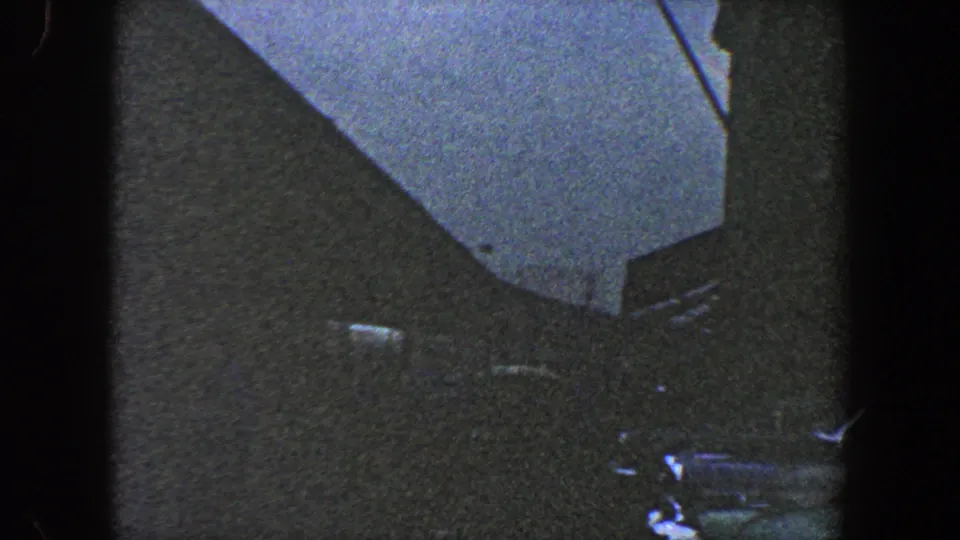 1960 New York City 8mm frame showing a dark building corner, pale sky, and a thin pole or antenna near the roofline.