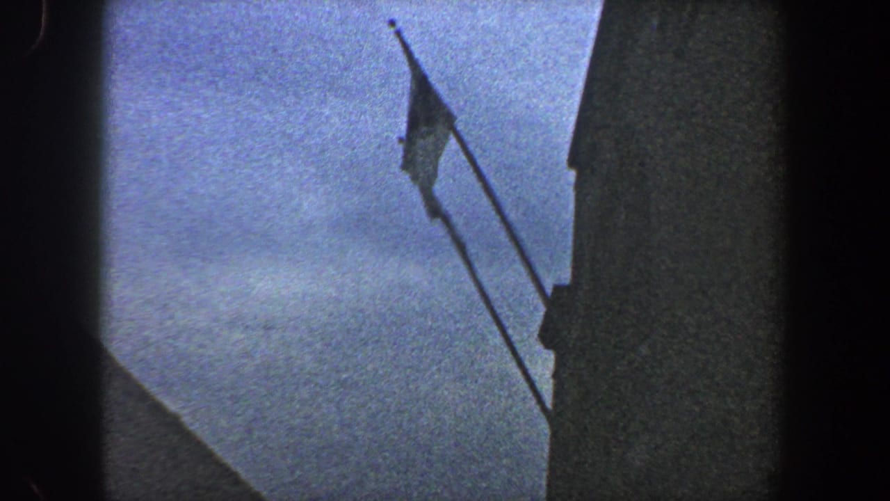 Flagpole and small flag beside a shaded building against blue sky.