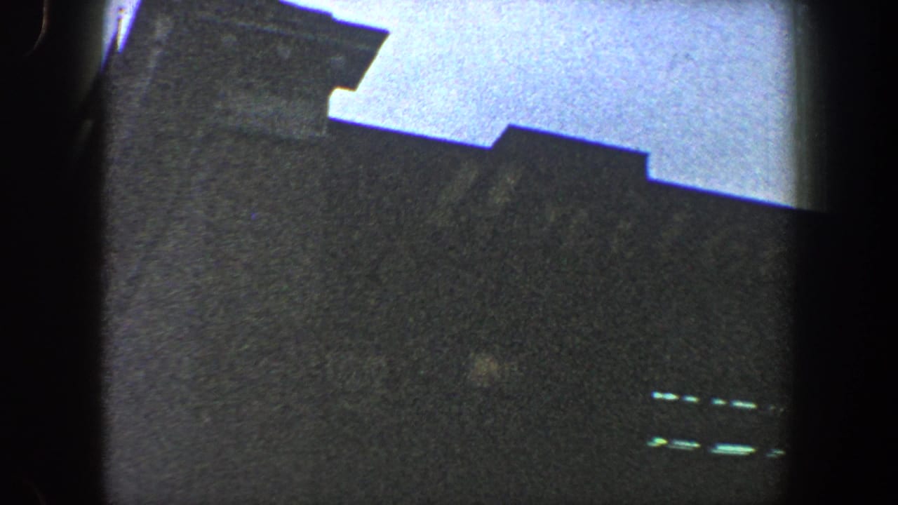 Dark roofline or stadium edge silhouetted below a pale sky with heavy film borders.