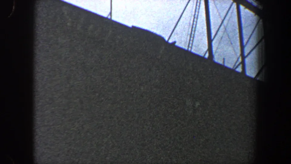 Shadowed New York City industrial structure with angled supports and cables against a washed pale sky, filmed on 8mm in 1960.