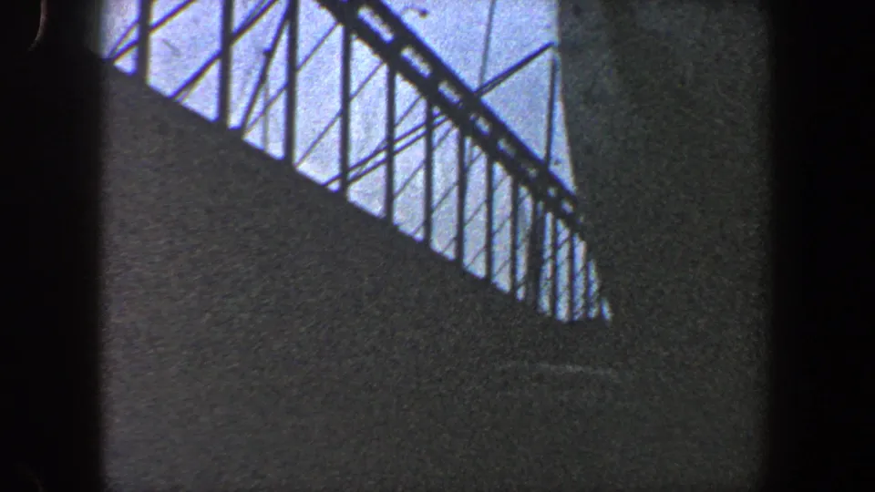 Late frame from a 1960 New York City 8mm pan showing silhouetted beams and cables over a dark industrial surface.