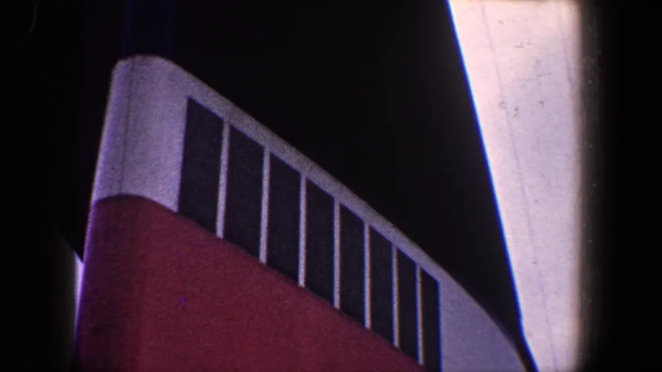 1960 New York City home-movie frame of red painted industrial architecture with white railings and a dark upper background.