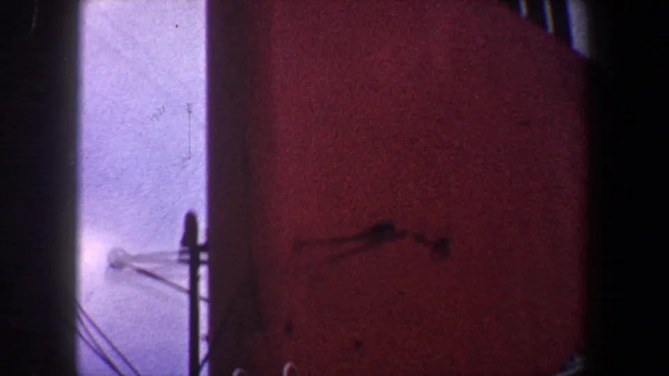 Low-angle 1960 New York City 8mm view of a red industrial surface beside a pale vertical plane and small attached fixtures.
