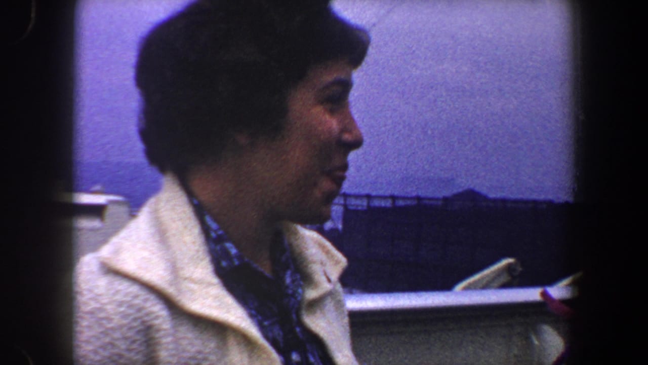 Woman in a white coat seen in profile beside a red smokestack and pale railing.